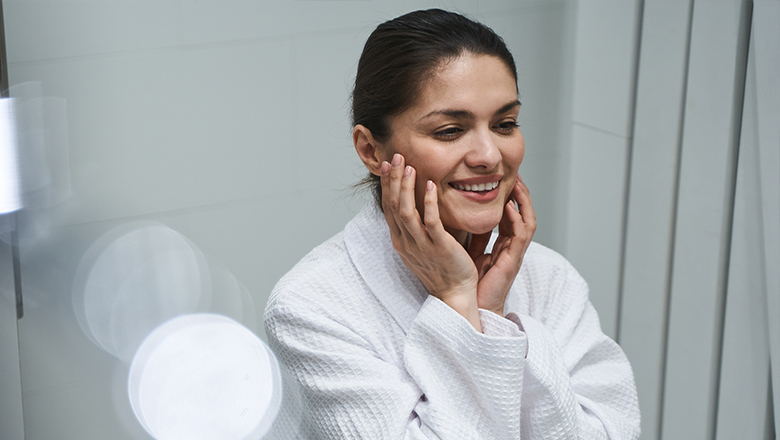 photo of a woman touching her face while looking in a mirror