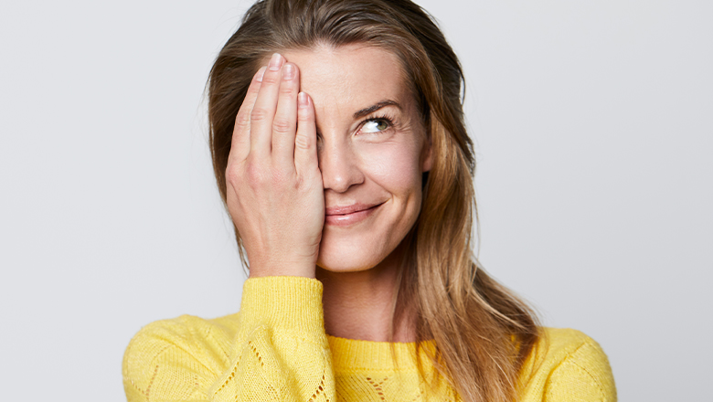 smiling woman with hooded eyelids covering one eye with hand